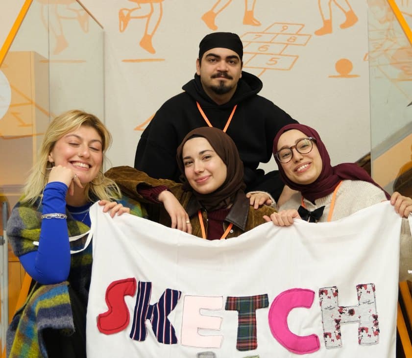 Sketch ekibi, kumaştan harflerle yazılmış SKETCH pankartıyla