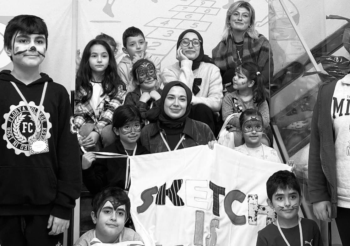 Yüzleri boyanmış çocuklar ve Sketch gönüllüleri, SKETCH pankartıyla